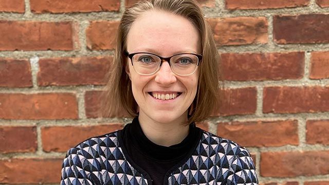 smiling woman in glasses in front of brick wall.